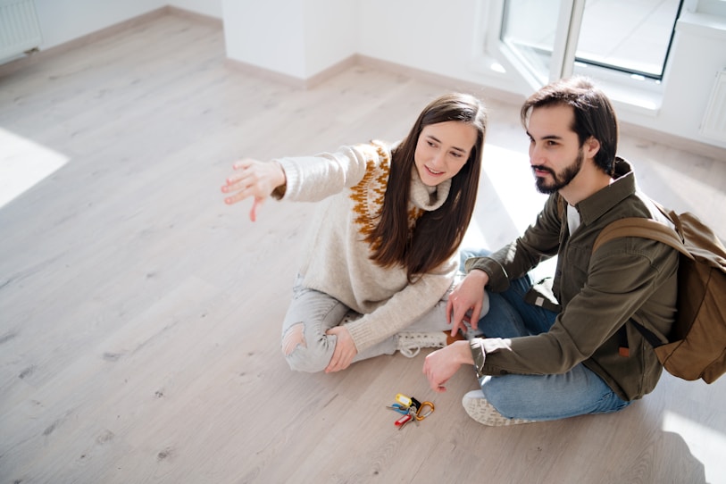 Young couple sitting on a wooden floor in an unfurnished room