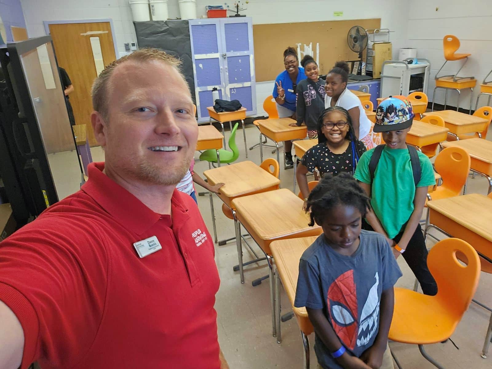 Man taking selfie in a classroom with kids and desks in the background