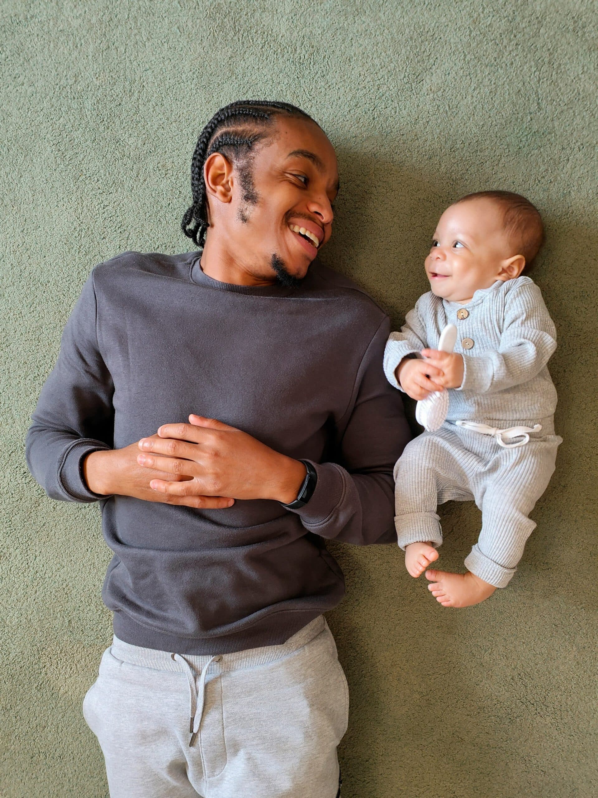 Young man and baby lying on a carpeted floor smiling at each other