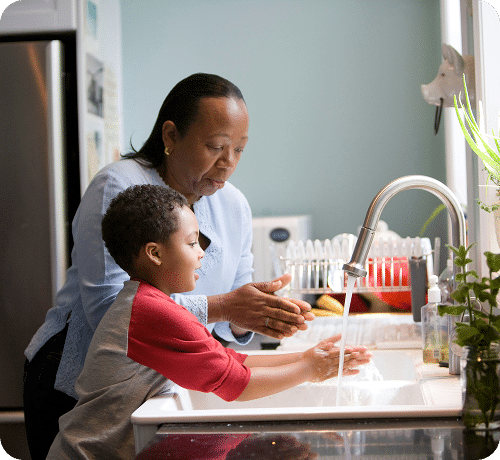 Young boy and older woman washing hands in a sink in a bright clean kitchen