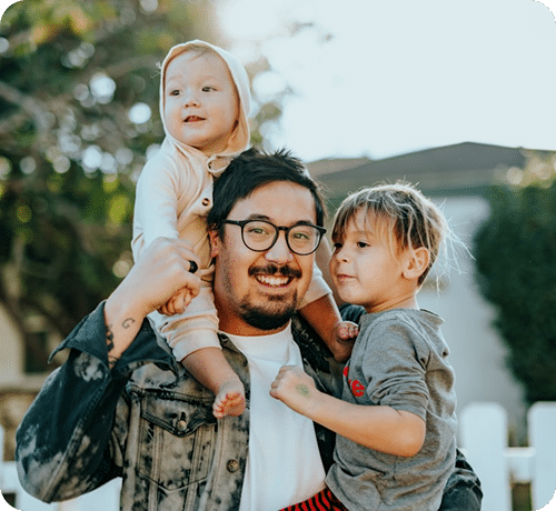 A smiling father holding two young children in the outdoors