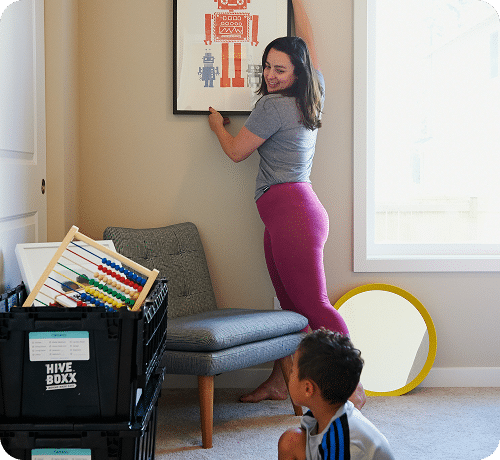 A woman hanging a framed poster in a living room
