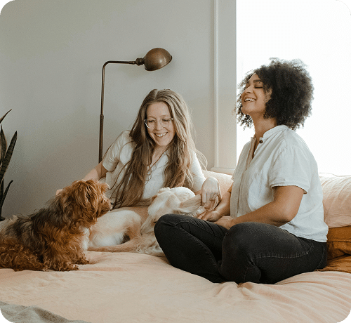 Two women sitting on a bed with two dogs